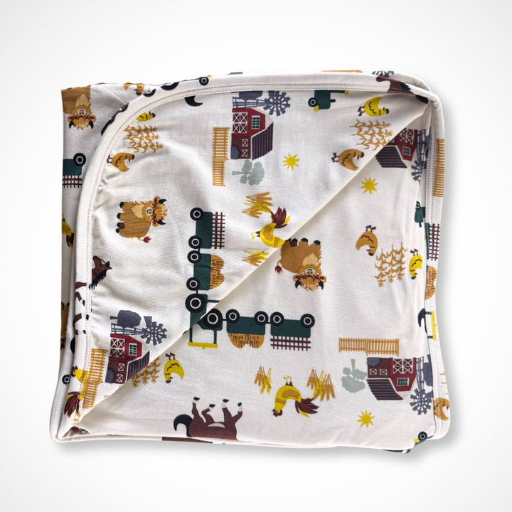 Folded bamboo baby blanket with animal and train pattern on a white background