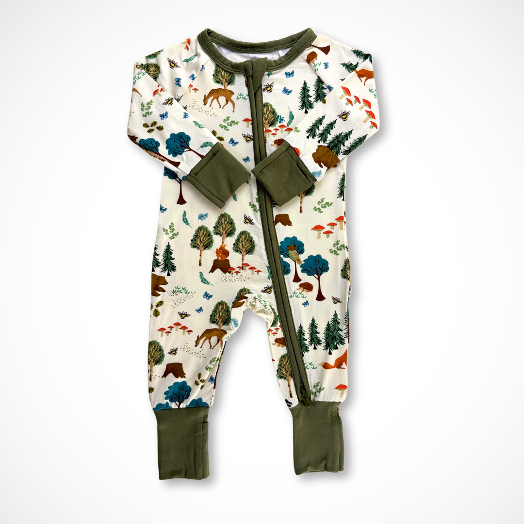 Long-sleeve zip up baby pajama in bamboo fabric. The Into the Woods print features trees, mushrooms, and forest friends such as deer, squirrels, bears, foxes, and hedgehogs, in earthy tones. The pajama cuffs and trim are olive green.