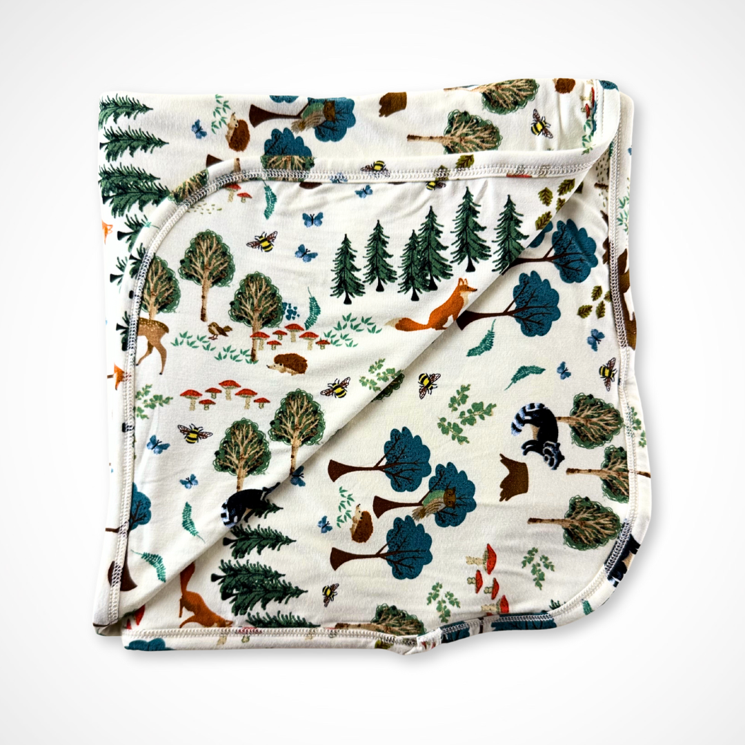 Folded bamboo blanket with forest pattern featuring trees, animals, and plants on a white background