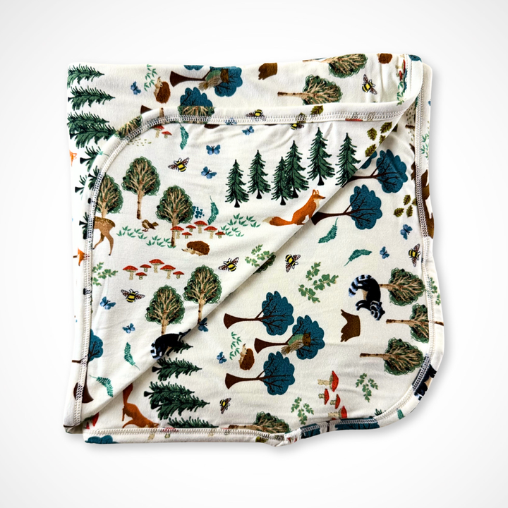 Folded bamboo blanket with forest pattern featuring trees, animals, and plants on a white background